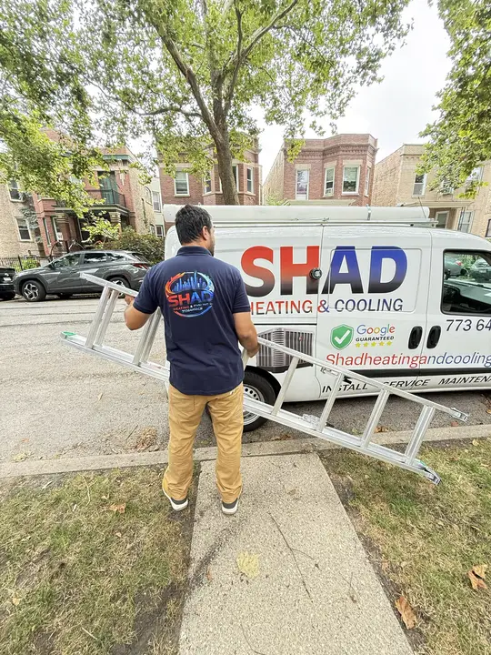 Shad Heating and Cooling technician carrying a ladder past the company van on a Chicago street